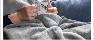 A woman with a mug of drink covered herself with a flannel blanket
